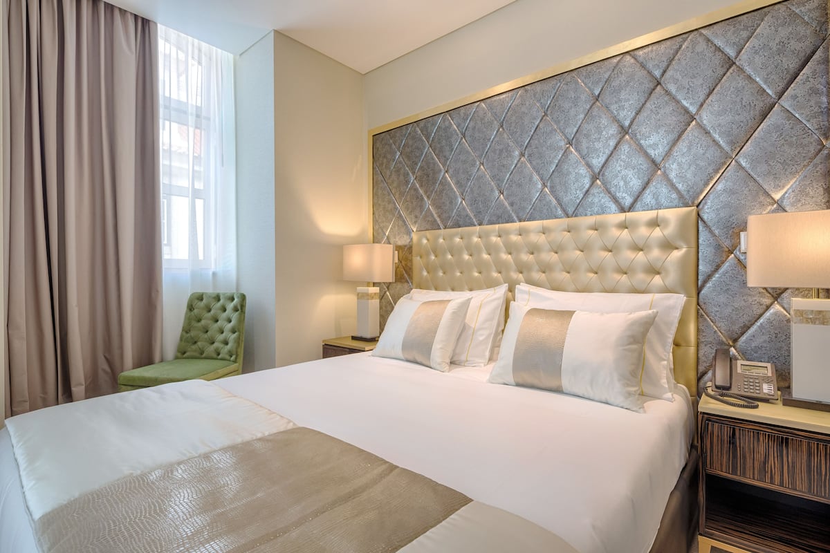 A hotel room with a large bed, a green chair, a headboard with a diamond pattern, and a bedside telephone.