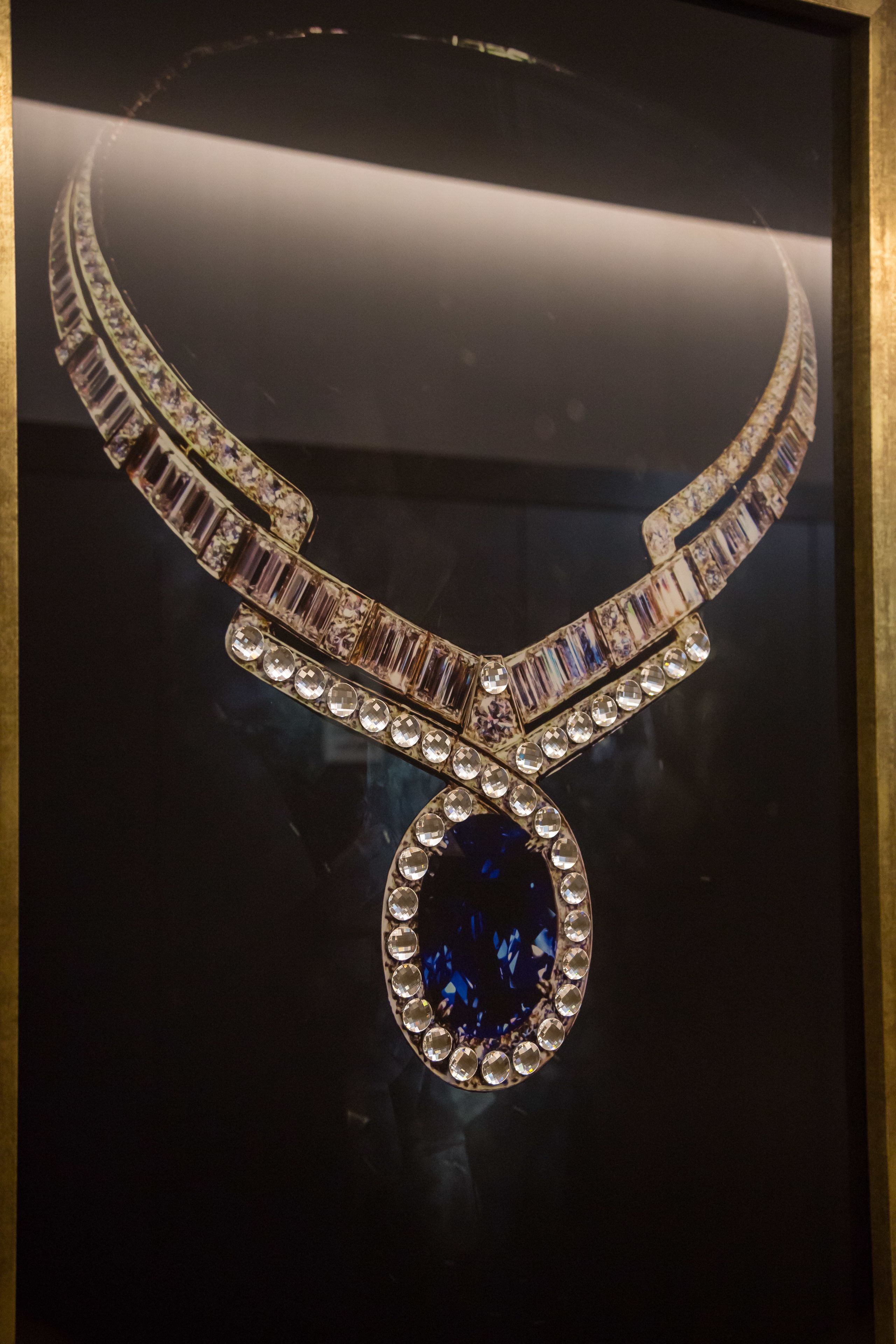 Un collier orné d’une grande pierre précieuse centrale et de pierres plus petites disposées le long du fermoir, présenté dans un écrin sombre.