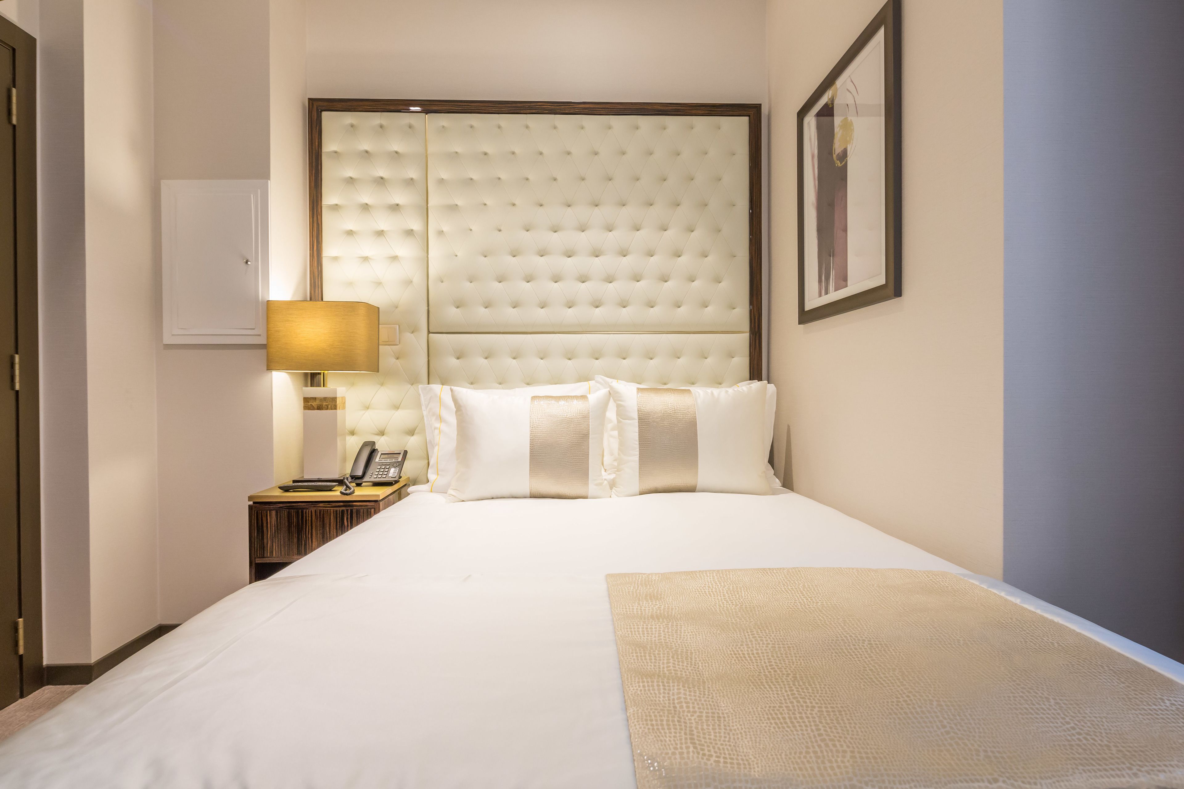 A hotel room with a large bed, a bedside lamp, a telephone, and a framed picture on the wall.