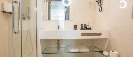 A modern bathroom with a glass shower enclosure, a white sink with a mirror above, and a toilet with a glass shelf.