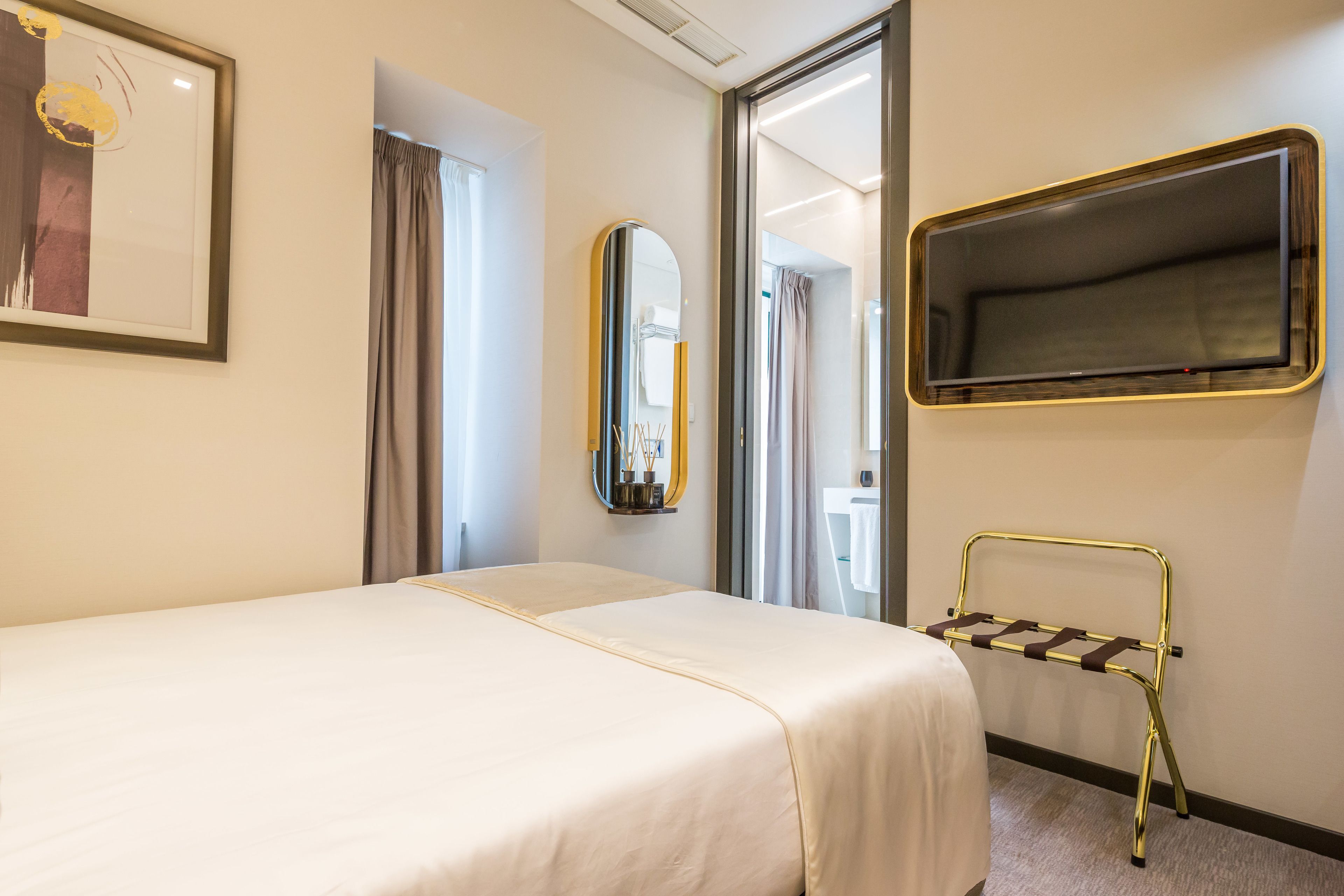 Une chambre d’hôtel avec un lit, un miroir, une télévision et une fenêtre.