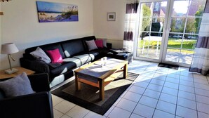 A living room with a black sofa, a wooden coffee table, and a painting on the wall. - Newly furnished holiday home near the dike well suited for families with WiFi (Dornum-Neßmersiel)