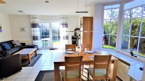 A modern living room with a sofa, coffee table, and dining area with chairs and a table set for two. - Newly furnished holiday home near the dike well suited for families with WiFi (Dornum-Neßmersiel)