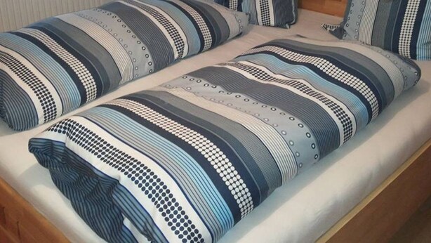 Una cama doble con ropa de cama a rayas y almohadas combinadas, un cabecero de madera y una ventana con cortinas.