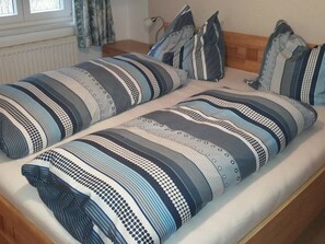 Una cama doble con ropa de cama a rayas y almohadas combinadas, un cabecero de madera y una ventana con cortinas.