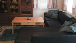 Una sala de estar con un sofá de color oscuro, una mesa de centro de madera y un mueble con puertas de vidrio.
