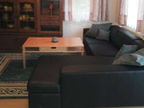 Una sala de estar con un sofá de color oscuro, una mesa de centro de madera y un mueble con puertas de vidrio.