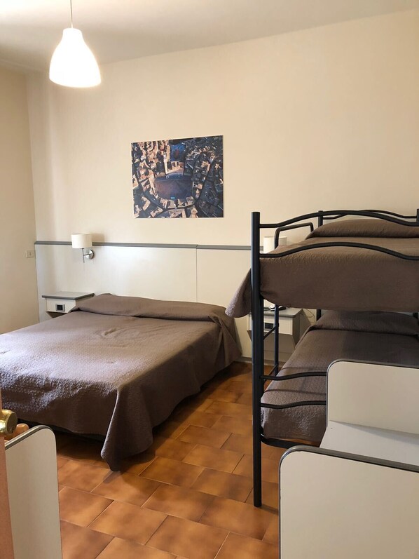 A dormitory room with bunk beds, a single bed, a wall-mounted lamp, and a cityscape painting. - Hotel Ai Tufi (Siena)