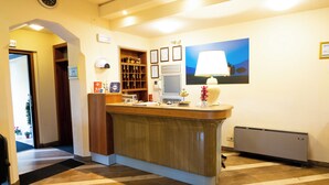 Un área de recepción con mostrador de madera, un reloj, certificados enmarcados, un cuadro y un radiador.