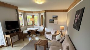 A living room with a TV, sofa, armchair, and a dining table. - (2) FeWo Bergveilchen, Zwei-Raum-Wohnung, ca. 43 qm, mit Terrasse (Reit im Winkl)