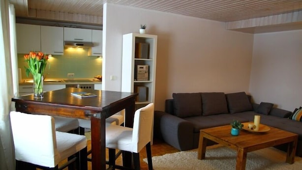 A modern living room with a sofa, a coffee table, and a dining area with chairs and a small table. - Vacation apartment Thann (Brannenburg)