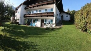 A two-story building with a sloped roof, a balcony on the upper floor, and a well-maintained lawn in front. - Vacation apartment Thann (Brannenburg)