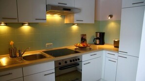A kitchen with white cabinets, a stainless steel sink, a stove, and a coffee maker. - Vacation apartment Thann (Brannenburg)