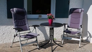 Two foldable patio chairs with cushions, a small round table, and a red flower vase. - Vacation apartment Thann (Brannenburg)