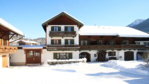 Ein traditionelles Chalet mit Schneedach, Steinfassade und mehreren Balkonen.