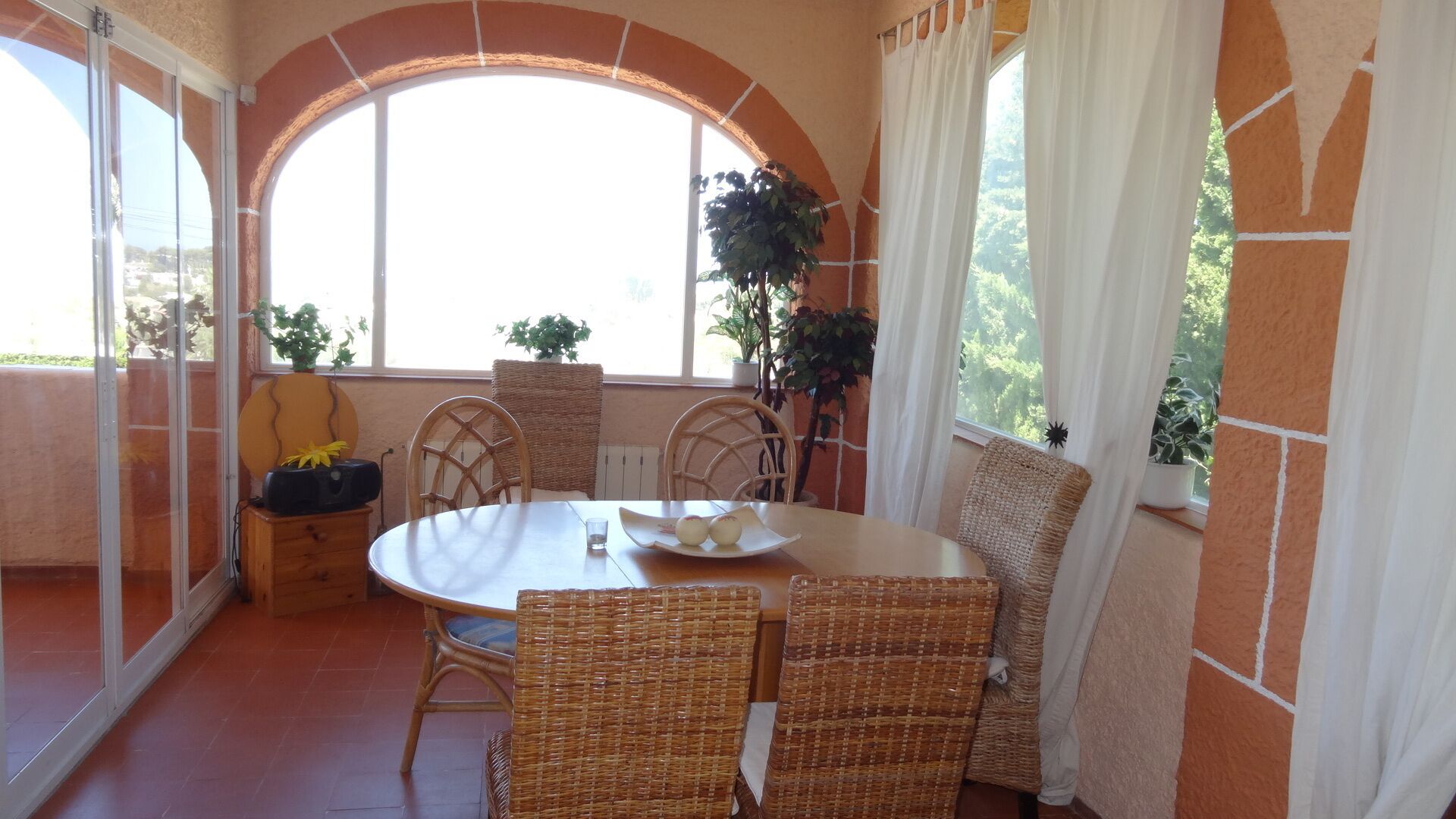 A dining area with a round table, wicker chairs, and potted plants.
