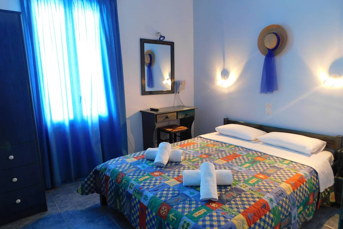 A hotel room with a bed, a desk, a chair, a mirror, and a window with curtains.