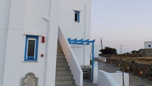 A white building with blue accents, a stone staircase, and a view of the surrounding area. - Studio Elisabeth (Tinos)