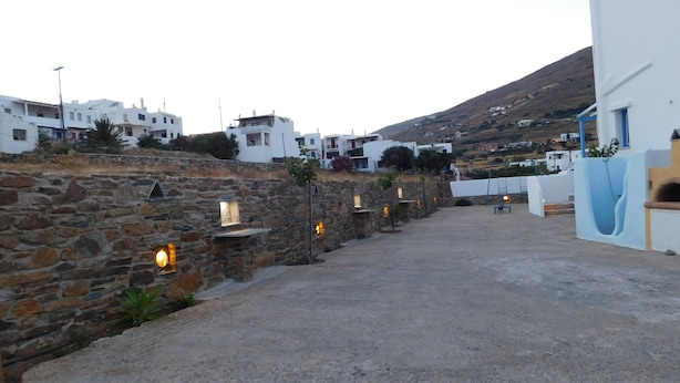 A coastal village with stone walls and white buildings, featuring a paved pathway and a small seating area. - Studio Elisabeth (Tinos)