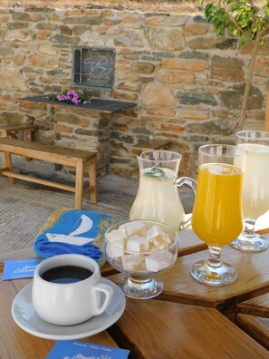 A table with a cup of coffee, a pitcher of milk, a glass of orange juice, and a bowl of ice cubes. - Studio Elisabeth (Tinos)