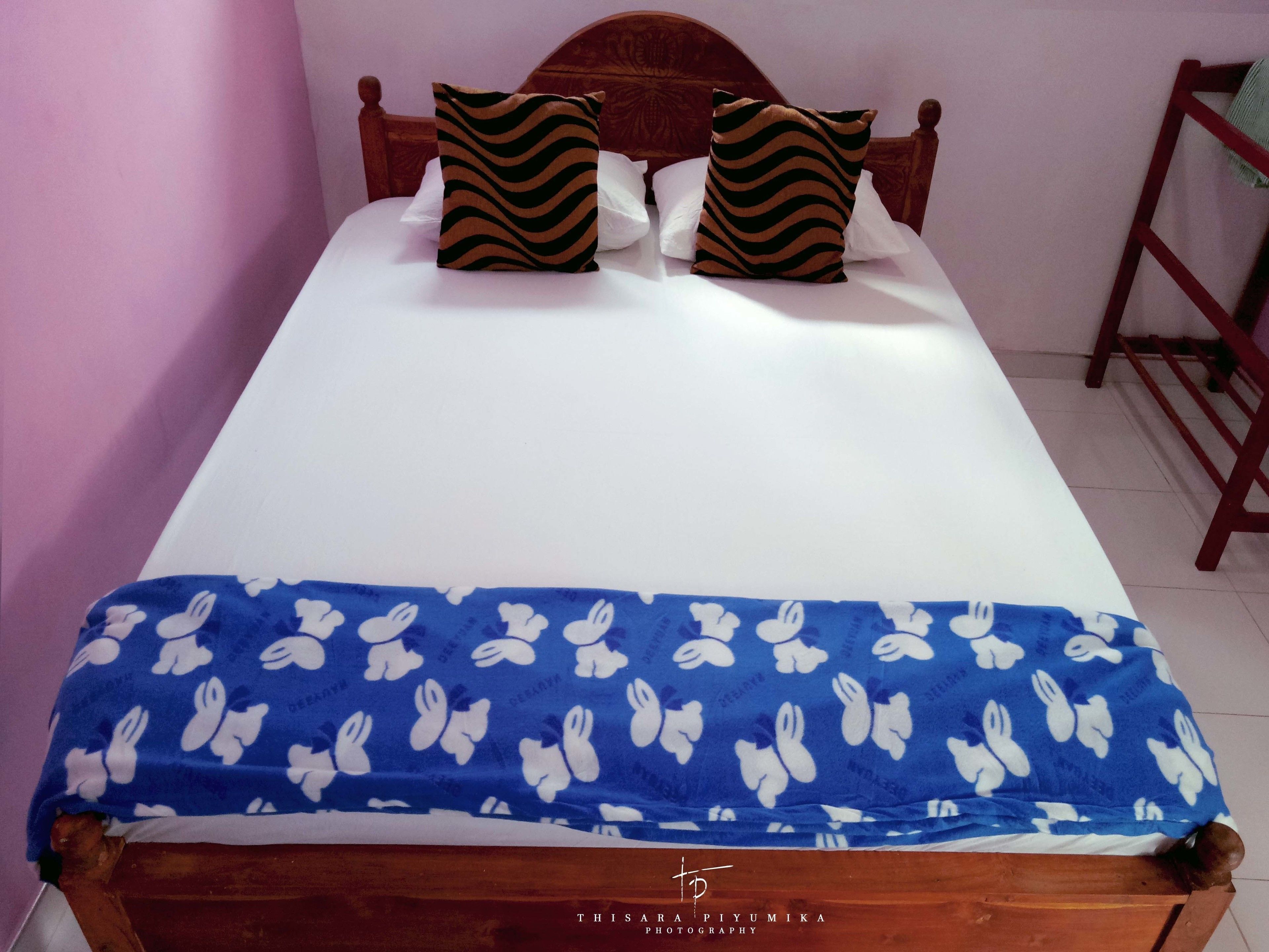 A bed with a white sheet, two patterned pillows, and a blue blanket with white bunny prints.