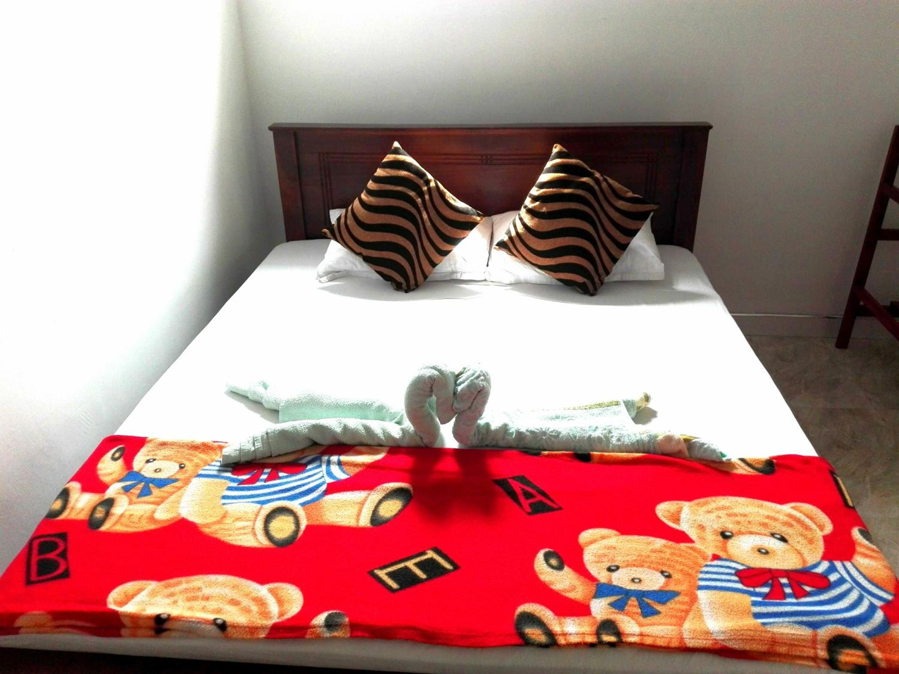 A bed with striped pillows, a red bear-themed blanket, and a wooden headboard.