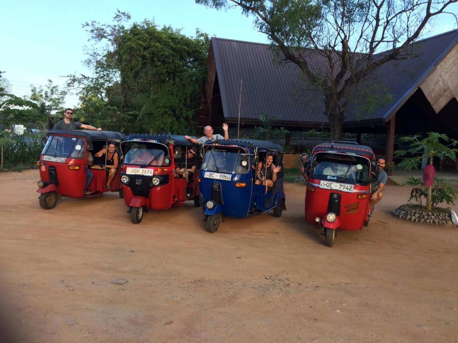 Three auto rickshaws parked in a line on a dirt road with a building in the background.