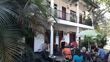 An outdoor seating area with tables and chairs, surrounded by palm trees and a covered balcony.
