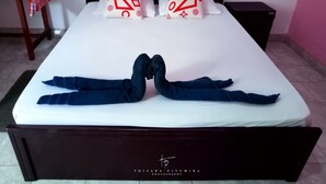 Ein ordentlich gemachtes Bett mit zwei Kissen, ein kleiner Tisch mit rot-weiß kariertem Tuch und ein dunkler Nachttisch.