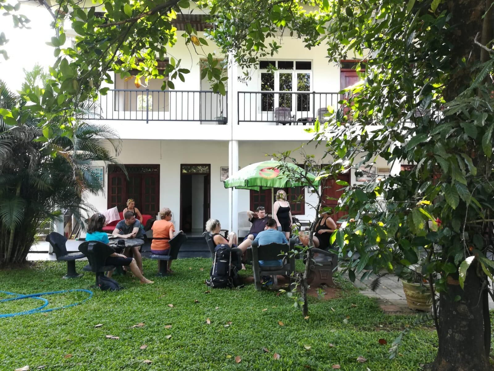 An outdoor seating area with people, a small tree, and a building in the background.