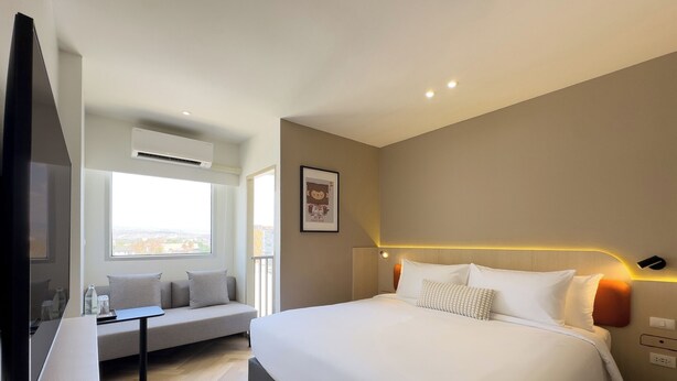 Ein modernes Hotelzimmer mit einem großen Bett, einer Couch, einem Fernseher und einem Fenster mit Blick auf die Stadt.