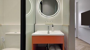 Ein modernes Badezimmer mit einem weißen Waschbecken, einem Spiegel mit rundem Rahmen und einem Handtuchregal mit Handtüchern.
