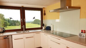 Cozinha com armários brancos, lava-louças de aço inoxidável, pia dupla e janela com vista para uma paisagem verde.