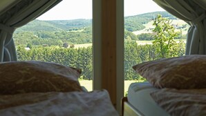 Quarto com duas camas, cada uma com almofadas estampadas, e uma janela grande com vista para uma paisagem arborizada.