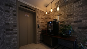 Un ascensor modern amb pantalla digital, sòl de marbre i paret de maó amb lluminàries penjants.