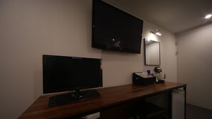 Habitació d'hotel amb escriptori de fusta, televisió de pantalla plana, mirall i nevera petita.