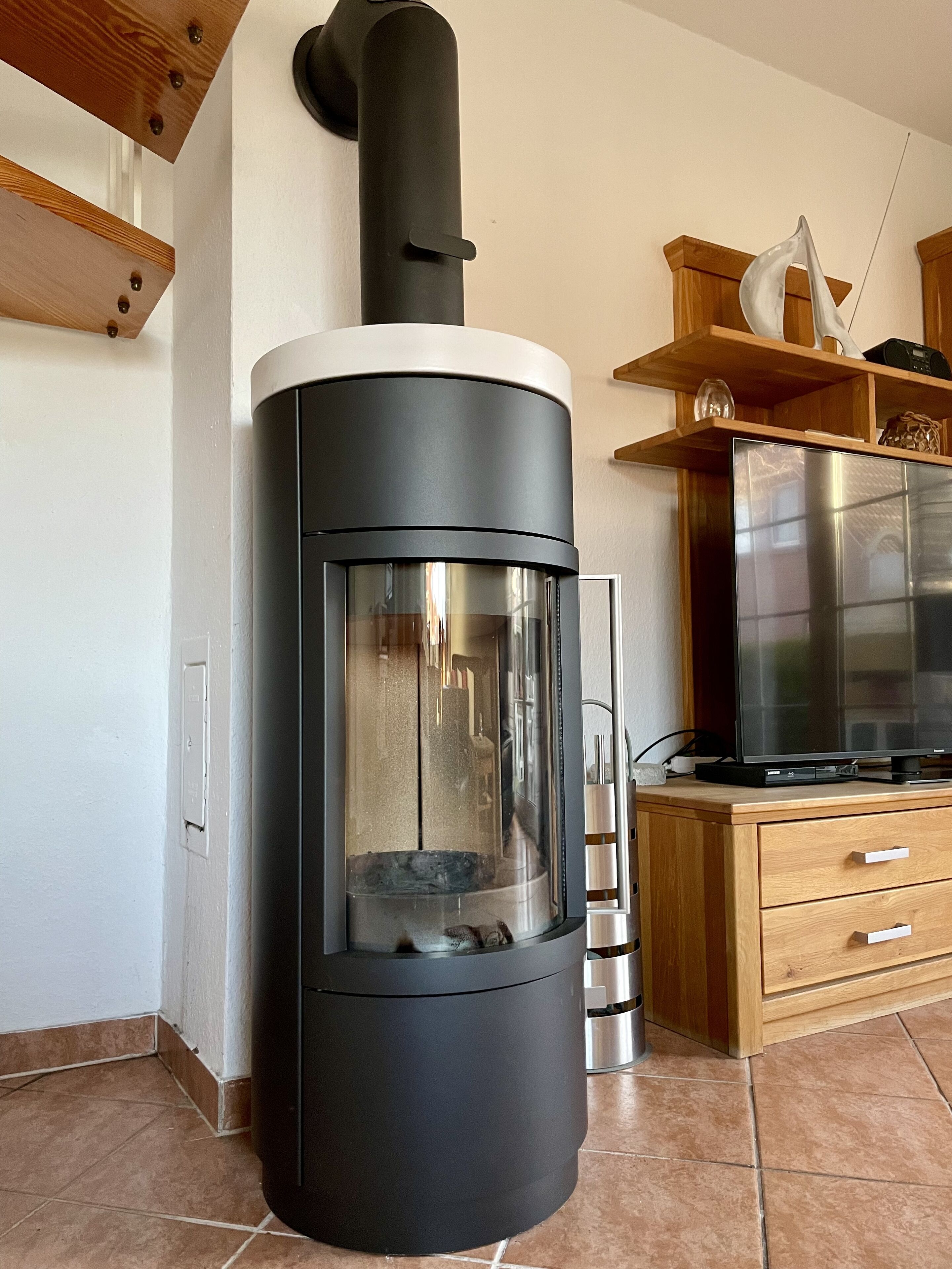Una cocina moderna con un estufa de leña negra, un refrigerador de acero inoxidable y armarios de madera.