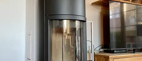 Una cocina moderna con un estufa de leña negra, un refrigerador de acero inoxidable y armarios de madera.