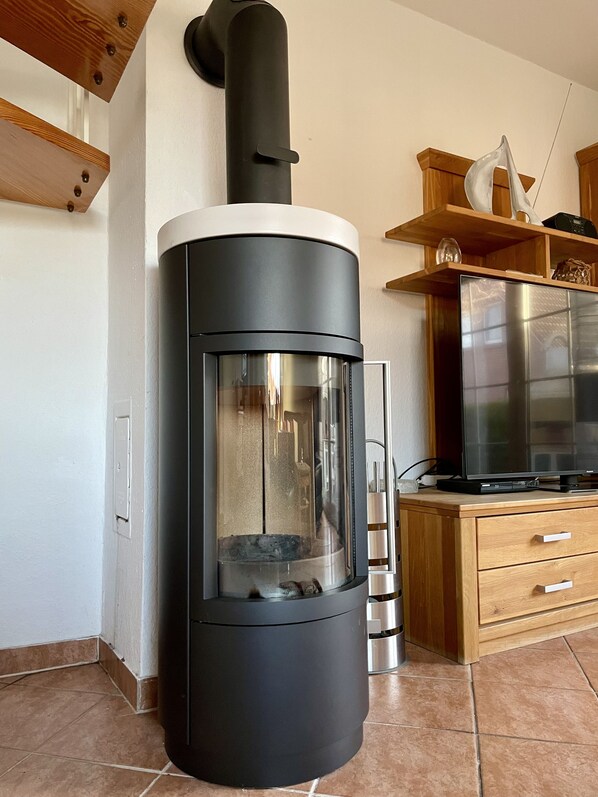 Una cocina moderna con un estufa de leña negra, un refrigerador de acero inoxidable y armarios de madera.