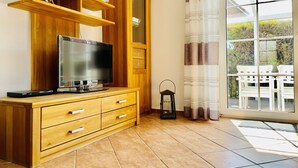 A wooden entertainment unit with a flat-screen TV, a radio, and a small decorative item. - Vacation home in Neßmersiel, quiet cul-de-sac location, close to the dyke (Dornum-Neßmersiel)