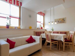 A dining area with a table, chairs, a sofa, and a window with plants.