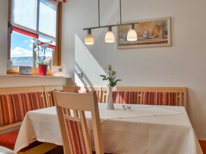 A restaurant interior with a table, chairs, a bench, a vase with flowers, a painting on the wall, and a window with a view. - Apartment with balcony - Panorama Apartments Thiem (Waischenfeld-Siegritzberg)