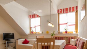 Ein modernes Wohnzimmer mit Fernseher, Sofa, Esstisch und Stühlen.