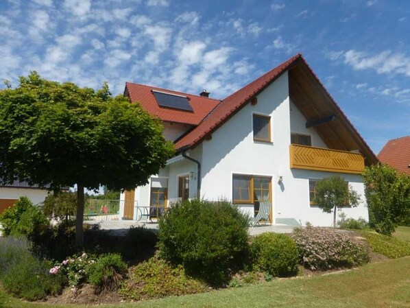 Une maison à deux étages avec un toit rouge, des murs blancs et un petit balcon.