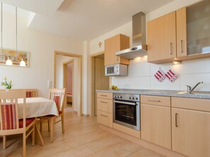 A modern kitchen with wooden cabinets, a built-in microwave, oven, and a stainless steel range hood. There is a dining area with a table and chairs. - Apartment with balcony - Panorama Apartments Thiem (Waischenfeld-Siegritzberg)