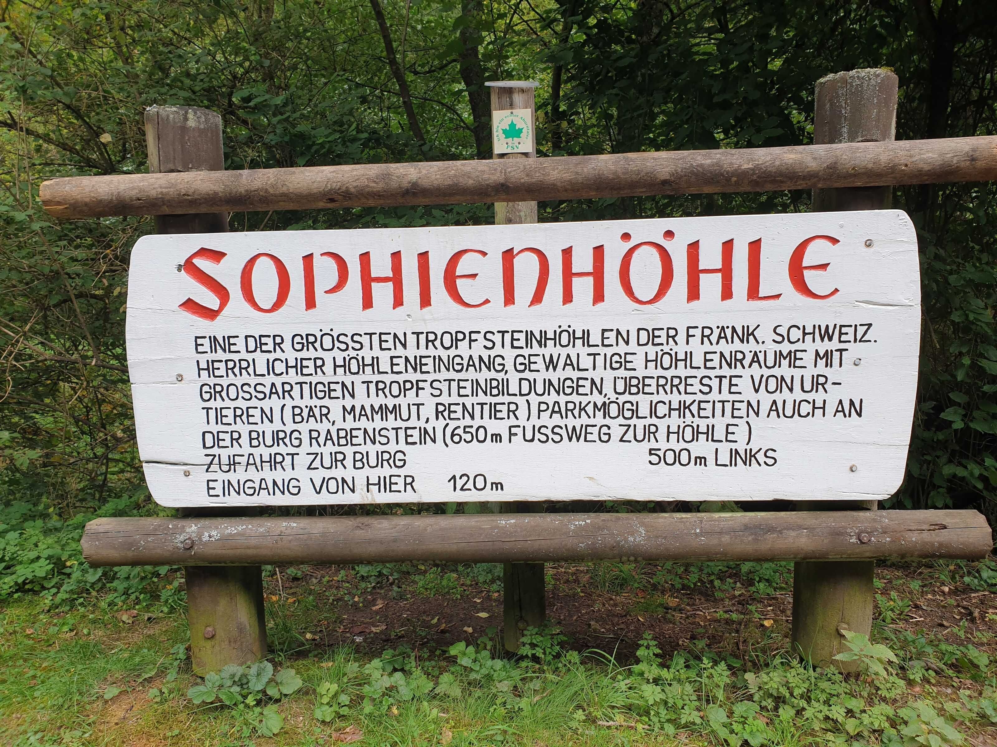Een bord met de naam 'Sophiehöhle' en informatie over een natuurlijke warmwaterbron in Frankrijk, Zwitserland.