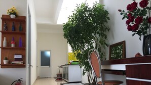 Un vestíbulo de hotel con una recepción, una planta en maceta, un extintor y una estantería con objetos decorativos.