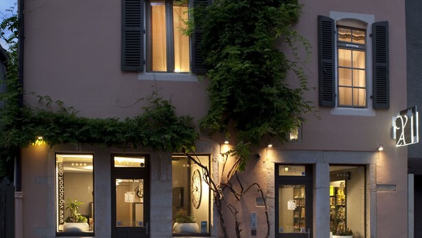 Un edificio de fachada rosa, con múltiples ventanas y contraventanas, y un gran árbol que crece a un lado.