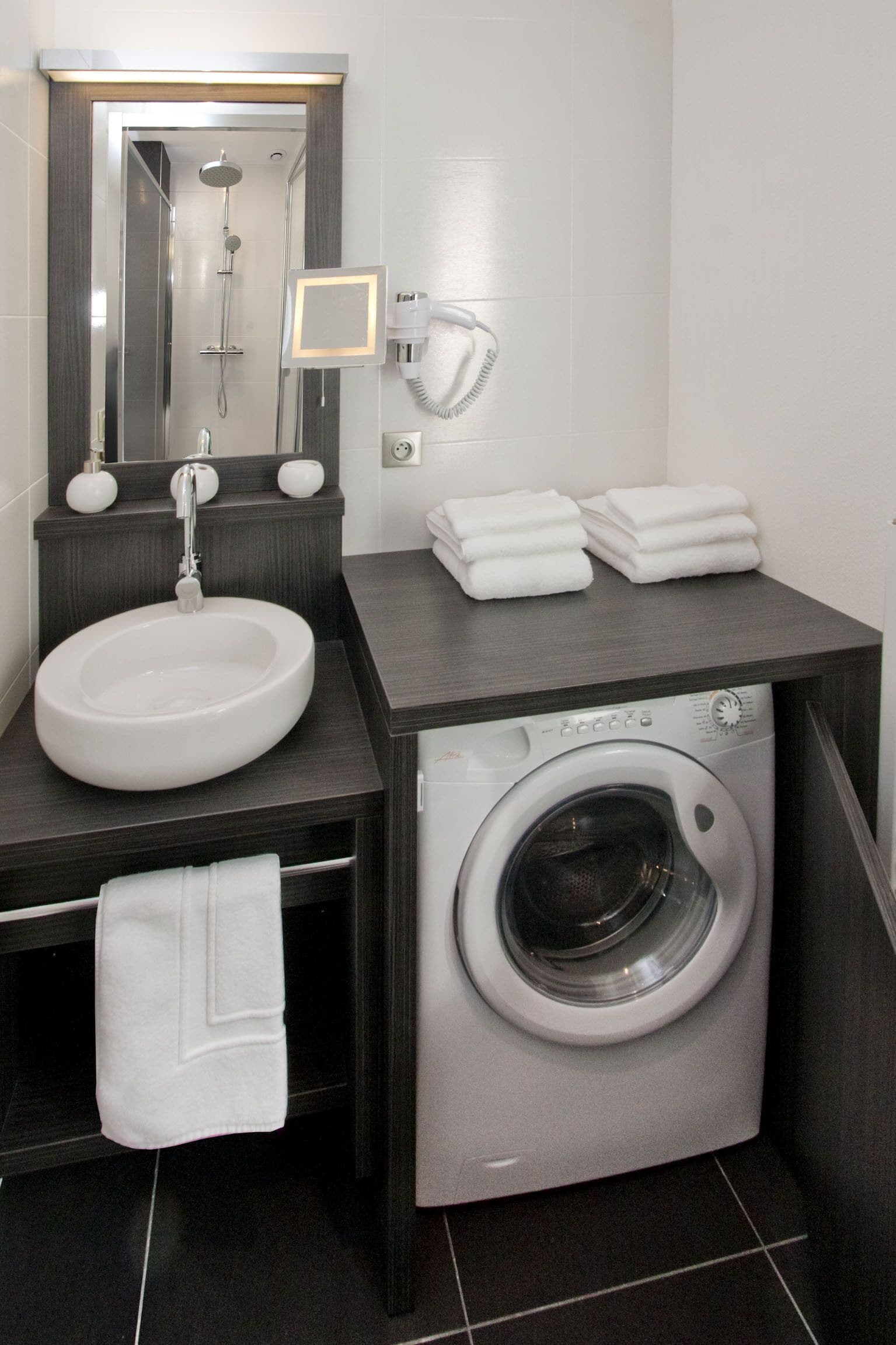 Un baño pequeño con lavamanos, espejo, toallero y lavadora.