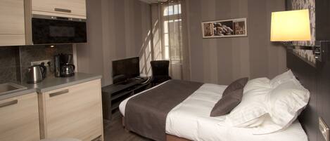 A hotel room with a bed, a desk, a chair, a coffee maker, and a TV.